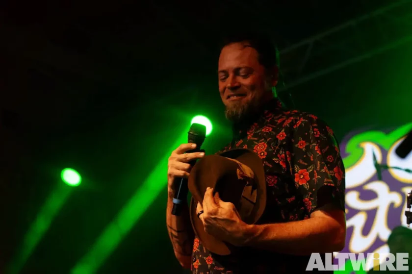 Man singing on stage with green lighting. Vocalist of Fortunate Youth.